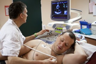 Мъж, който има ехокардиограма, със сензори, прикрепени към гърдите и изображение на монитор